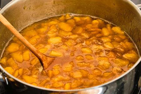 Cooking peach fruit in metal pot and stir with wooden spoon preparing homemade marmaladeの写真素材
