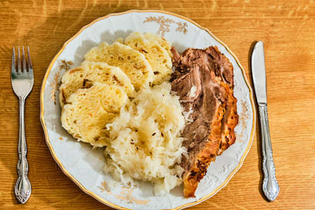 Traditional tasty czech food "knedlo vepro zelo" pork meat with dumplings and gabbage. On white plate on wooden table.の写真素材