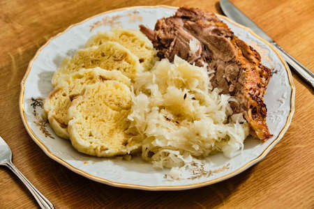 Traditional tasty czech food "knedlo vepro zelo" pork meat with dumplings and gabbage. On white plate on wooden table.の写真素材
