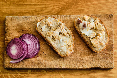 Tasty bread with lard, greaves and red onion on cutting board on wooden table