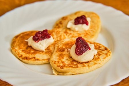 Tasty homemade pancakes with cheese cream and plum marmalade on white plate on wooden table