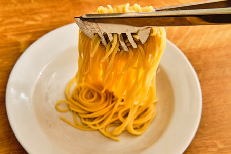 Putting tasty spaghetti on white plate on wooden table with toolの写真素材