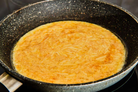 Cooking tasty homemade omellette with cheese on frying pan on stoveの写真素材
