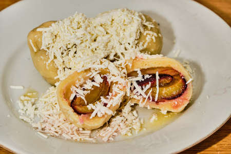 Tasty homemade curd (cream cheese) dumpling stuffed with plums with hard curd, sugar and melted butter on white plate on wooden tableの写真素材