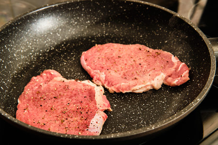 Cooking raw pork meat spiced steak on frying pan