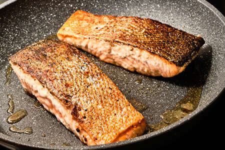 Cooking tasty salmon filet with skin on frying pan with oil on stoveの写真素材