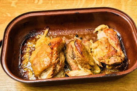 Tasty roast pork knuckle meat on roasting pan on wooden table