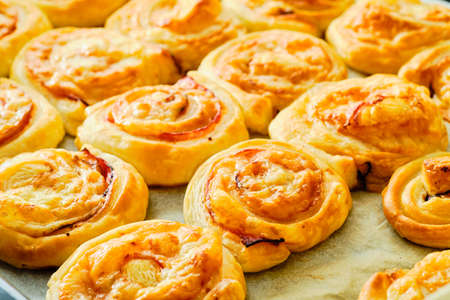 Fresh tasty puff pastry rolls with ham and cheese on baking trayの写真素材