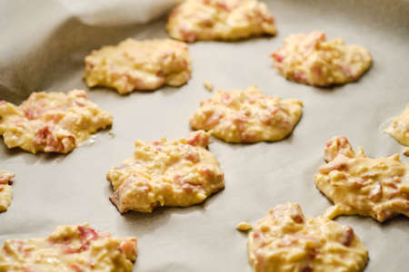 Preparing tasty gluten free cheese patties with dried ham on baking paper on trayの写真素材