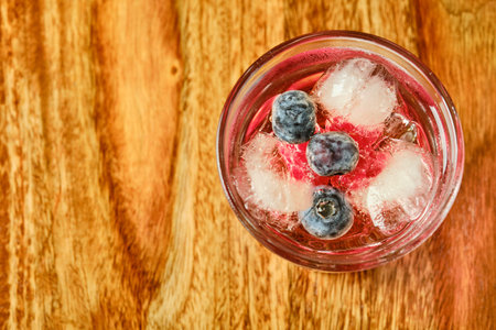 Tasty forest fruit coctail in glass with ice on wooden table with bilberries and raspberries top view with copy spaceの写真素材