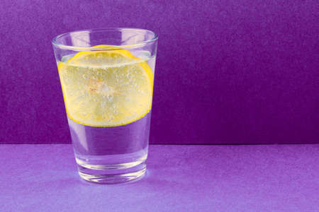 Mineral water with lemon in glass on purple backgroundの写真素材