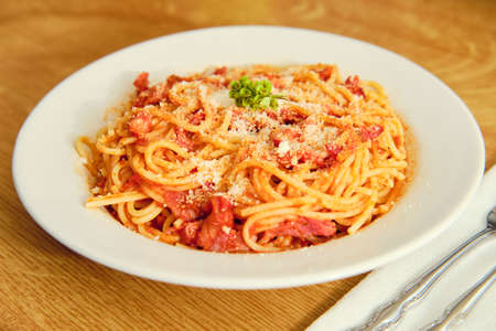 Tasty spaghetti with tomato sauce and dried ham on white plate on wooden table with servingの写真素材