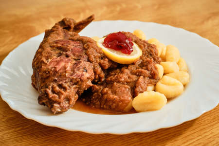 Tasty rabbit leg with wine vegetable gravy and gnocchi on white plateの写真素材