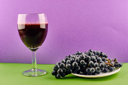 Tasty fresh red grape juice in glass with fruit on modern purple and green backgroundの写真素材