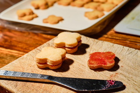 Spread currant jam on christmas cookie with knife on wooden cutting board