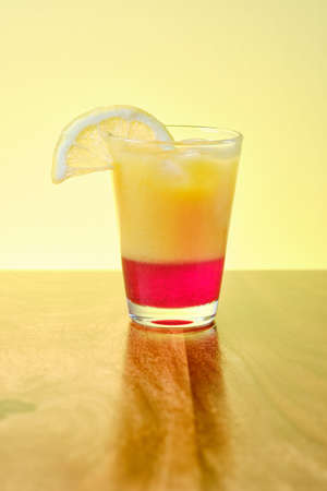 Fresh summer alcohol free  on beach drink with orange and red fruit juice in glass with ice and slice of lemonの写真素材