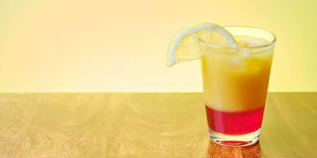 Fresh summer alcohol free  on beach drink with orange and red fruit juice in glass with ice and slice of lemonの写真素材