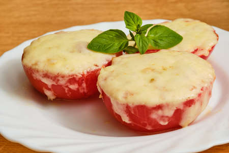 Tasty oven baked sliced tomatoes with melted cheese and oregano herb on white plateの写真素材