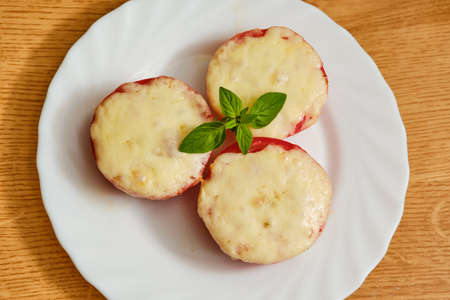 Tasty oven baked sliced tomatoes with melted cheese and oregano herb on white plateの写真素材