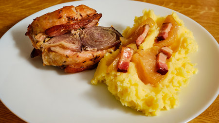 Tasty roast pork loin with red onion and bacon with mashed potatoes and apples on a white plateの写真素材