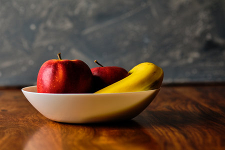 Still life with red apples and banana fruit in bowl on wooden tableの写真素材