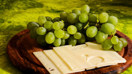 Tasty hard cheese with grape fruit on wooden cutting boardの写真素材