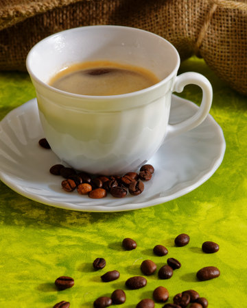 White cup of coffee with coffee beans and sack on green backgroundの写真素材