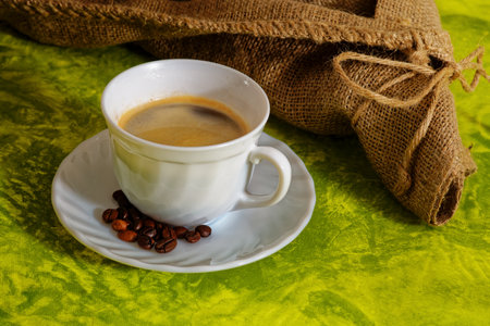 White cup of coffee with coffee beans and sack on green backgroundの写真素材
