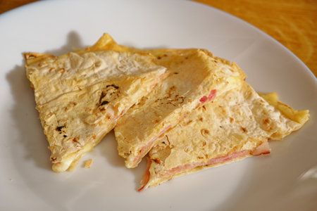 Tasty quesadilla with cheese and ham on white plateの写真素材