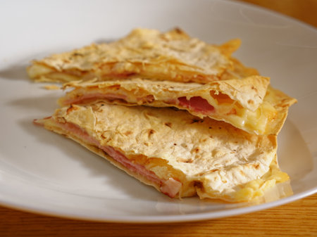 Tasty quesadilla with cheese and ham on white plateの写真素材