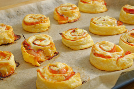 Tasty puff pastry pizza rolls on baking paper and trayの写真素材