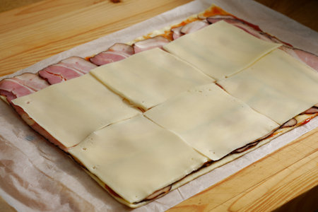 Puff pastry pizza rolls preparation - adding cheese on hamの写真素材