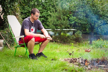 Young man grilling sausages on campfire.の写真素材
