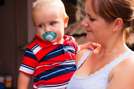 Beautiful smiling young mother holding cute toddler boy outdoors.