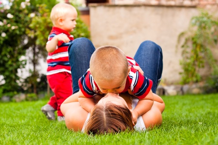 Happy mother kissing her son relaxing on the grass in the garden.の写真素材