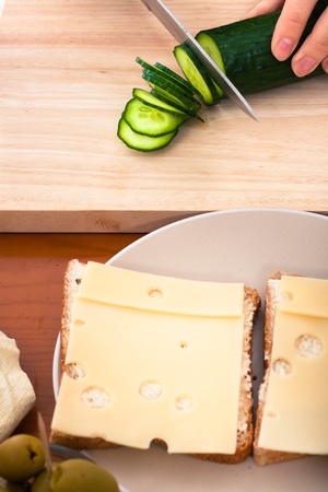 Detail of kitchen table with sandwiches and female hand chopping fresh cucumber.の写真素材