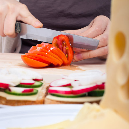 Detail of kitchen table female hands slicing fresh tomato.