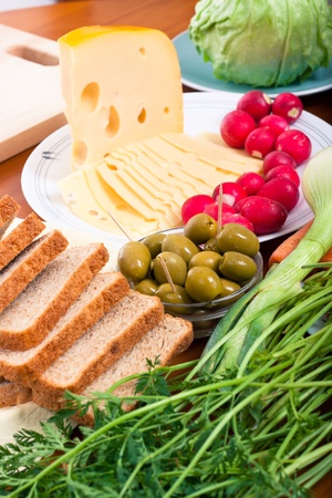 Detail of table with Emmenthal cheese, olives, bread and fresh vegetable.の写真素材