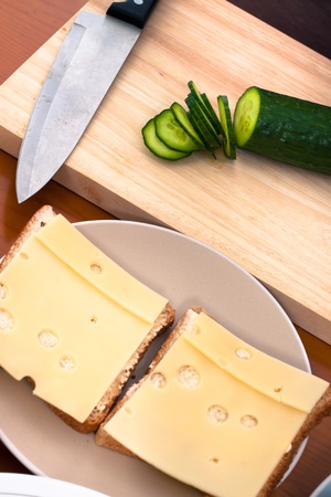 Detail of kitchen table with cheese sandwiches and chopping board with knife and sliced cucumber.の写真素材