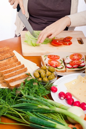 Detail of kitchen table and woman cutting fresh vegetable and making sandwiches.の写真素材