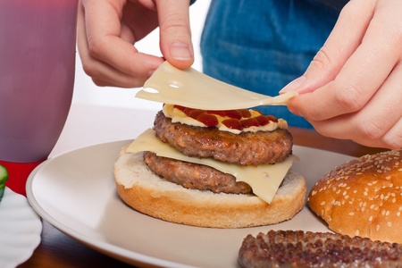 Close up of hands putting cheese on homemade double hamburger.の写真素材