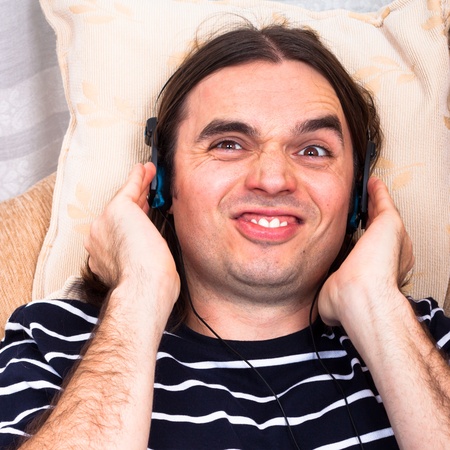 Young funny man with headphones listening music on sofa.の写真素材