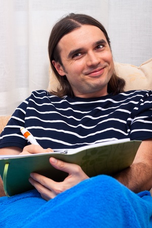 Young happy smiling man writing note to his diary and relaxing on sofa.の写真素材