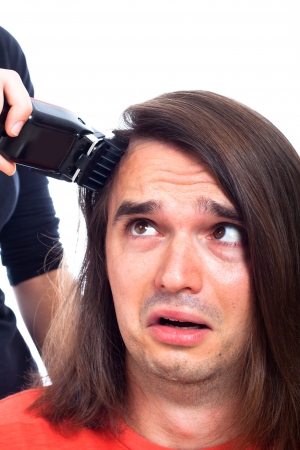 Close up of unhappy long haired man being shaved with hair trimmer, isolated on white background.の写真素材