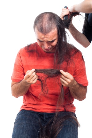 Unhappy bald man holding his long hair man and crying, being shaved with hair trimmer, isolated on white background.の写真素材