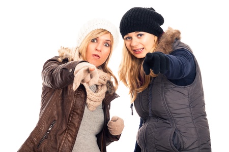 Two young surprised women in winter clothes pointing at you, isolated on white background.の写真素材
