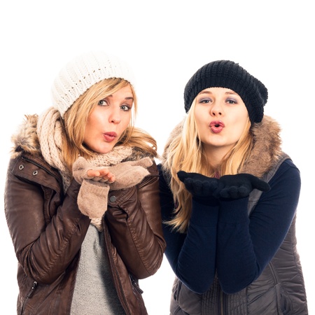 Two young happy women in winter clothes sending kiss, isolated on white background.の写真素材