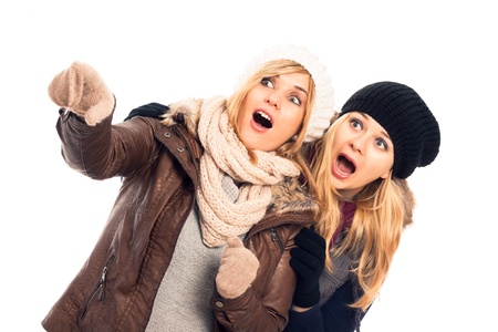 Two young shocked women in winter clothes pointing, isolated on white background.の写真素材