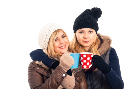 Two young happy women in winter clothes holding mug with hot drink, isolated on white background.の写真素材