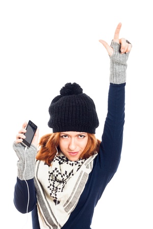 Young happy woman in winter clothes holding smartphone, listening music and pointing up, isolated on white background.の写真素材